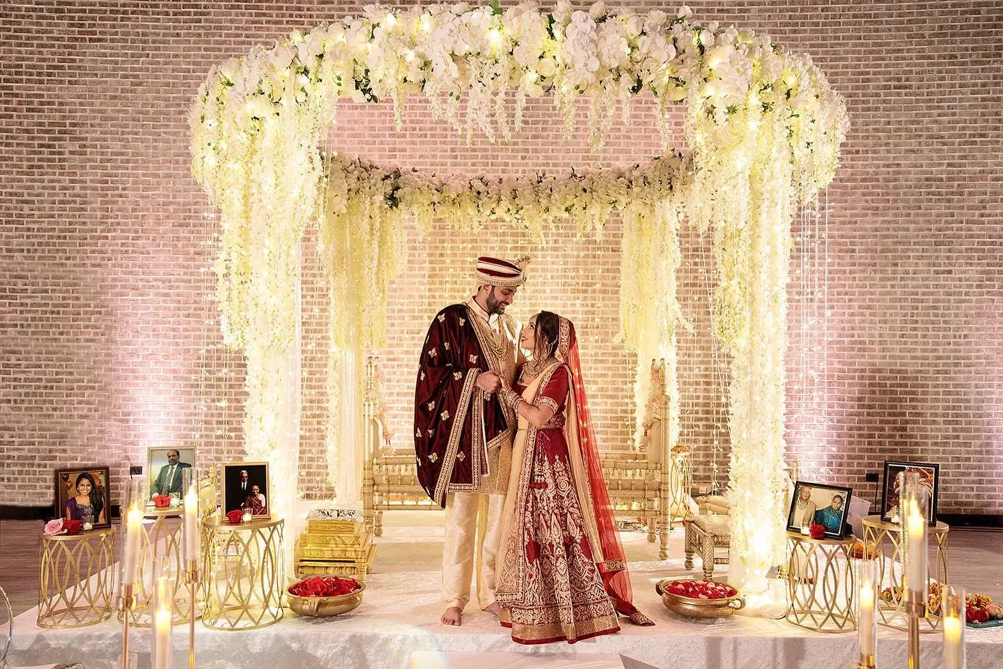 Bride and groom in red lehenga and sherwani under floral mandap